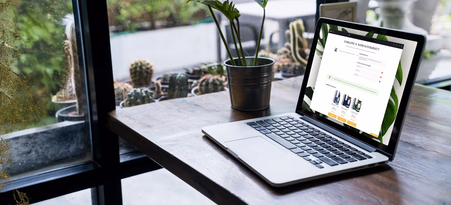 Laptop auf einem Holztisch neben einem Blumentopf, zeigt eine Webseite zur Einnahme und Kombinierbarkeit von Produkten.